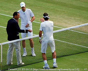 An umpire in a black coat flips a coin at the tennis net between to tennis players dressed in white.