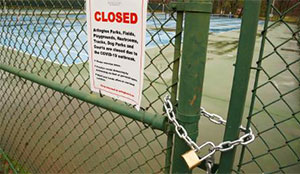 Closed sign on the gate of a tennis court that is chained shut.